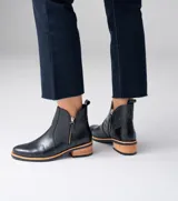 Botas cortas de cuero vacuno color negro, con diseño de doble cierre lateral y taco de madera foliado. Presentan una combinación de texturas en el cuero y una suela de goma contrastante.