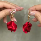 Aros de tipo argolla dorada con diseño retorcido, de los cuales cuelga un dije en forma de pétalo de flor en color rojo vibrante.