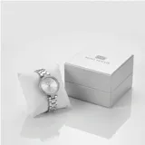 Reloj analógico de mujer con caja redonda de metal plateado y bisel decorado con cristales. Presenta una esfera minimalista con índices simples y una malla de eslabones de acero inoxidable con cierre desplegable.