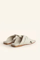 Sandalia tipo slide de cuero vacuno color blanco, con diseño de tiras cruzadas y fruncidas. Presenta una puntera cuadrada y una suela plana de cuero con un pequeño taco de 2 cm.