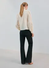 Blusa de color crema con cuello redondo, mangas largas abullonadas y detalles de bordado y puntilla vertical en el frente.