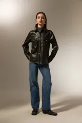 Sobrecamisa de cuero sintético en color negro, con cuello clásico, cierre frontal mediante botones metálicos y dos bolsillos frontales con solapa. Presenta costuras a la vista y mangas largas con puños abotonados.