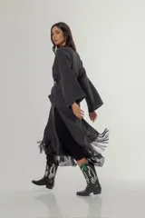 Saco largo de tejido de punto color gris oscuro, con mangas anchas, aberturas laterales y flecos largos en el ruedo. Presenta un diseño abierto que permite el uso de cinturón para entallar la silueta.