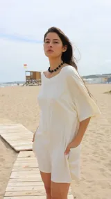 Mono corto de lino en color natural, con diseño versátil de cuello redondo y espalda escotada, o escote en V y espalda cerrada. Presenta mangas cortas holgadas y bolsillos laterales.