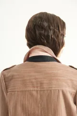 Chaqueta a rayas marrones y blancas de corte clásico, con cuello camisero, hombreras y detalles en tono liso negro y rosado en la parte posterior del cuello.