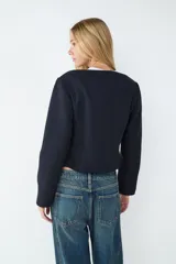 Campera corta de paño color negro, con escote redondo y manga larga. Presenta cierre frontal mediante tres ganchos metálicos decorativos. Diseño entallado con forro interior.