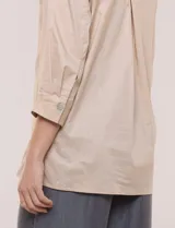 Camisa de silueta holgada y largo extendido, confeccionada en poplín elástico de color blanco. Presenta cuello solapa abierto en V con cartera frontal de abotonadura oculta, hombros caídos y mangas tres cuartos. Cuenta con espalda con canesú, pliegue central y ruedo recto con pequeñas aberturas laterales.