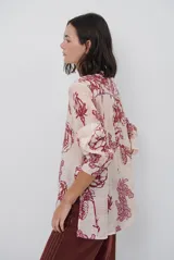 Camisa de corte holgado con estampado floral en tonos rojizos sobre base clara. Presenta cuello mao con escote en V y cierre frontal parcial con botones, además de mangas largas con puños ajustados.