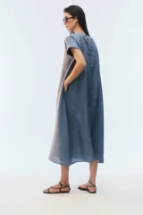 Vestido midi evasé color azul, confeccionado en lino, con escote redondo, mangas cortas con dobladillo vuelto y bolsillos laterales. Presenta un ruedo asimétrico, más largo en los laterales.