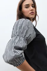 Remera de algodón negra con mangas abullonadas de tela con estampado vichy en blanco y negro, puños elásticos y cuello redondo.