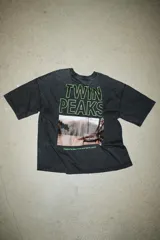 Camiseta de cuello redondo y manga corta con efecto lavado. Presenta una estampa frontal inspirada en la serie Twin Peaks con diseño de cortinas rojas y suelo geométrico.