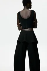 Pantalón negro de corte barrel con pollera mini acampanada superpuesta en la cintura, piernas amplias y cierre lateral.