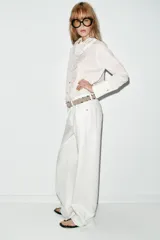 Camisa de manga larga con estampado de rayas verticales finas, cuello redondo con volante plisado y detalle de volante lateral en el frente. Cuenta con cierre frontal de botones y puños anchos.