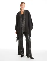 Ruana de tejido soft color negro, con detalles de brillos y tachas en los bordes frontales. Presenta una caída fluida y terminación con flecos.