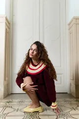 Buzo de punto bordó estilo oversize, con cuello babero amplio con volados y franjas en tonos amarillo y rojo, manga larga con terminación en volados.