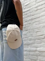 Gorro tipo gorra de béisbol color crudo con visera curva y logo bordado en el centro.