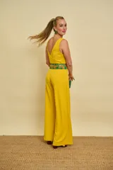 Enterito largo de color amarillo con escote en V cruzado, tirantes finos y pantalón de corte recto y holgado. Incluye un cinturón de tela estampado en tonos verdes y dorados.