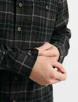 Camisa de franela a cuadros con cuello button-down, manga larga y botones de madera. Presenta dos bolsillos tipo parche en el frente con cierre de botón.