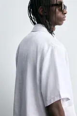 Camisa de manga corta confeccionada en tejido de cáñamo, con calce relajado. Presenta cuello solapa, cierre frontal con botones y dos bolsillos de plastrón en la parte inferior delantera.