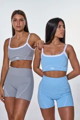 Conjunto deportivo compuesto por un top y un short de tiro alto en color gris. El top presenta breteles blancos, escote redondo y el logo de la marca estampado en el frente. El short cuenta con costuras decorativas blancas que realzan el diseño.