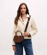 Cartera bandolera de tamaño mediano con cuerpo frontal en gamuza y laterales estructurados. Cuenta con asa corta superior, correa larga ajustable y desmontable, cierre metálico y bolsillo trasero aplicado.