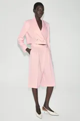 Blazer corto rosado con cuello solapa, hombreras y mangas largas. Cuenta con cierre cruzado delantero con dos botones oscuros y un bolsillo de ojal en el pecho.