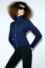 Chaqueta de punto acanalado azul marino con cuello alto y cierre frontal de cremallera metálica. Cuenta con detalles de rib en color blanco en los puños de las mangas largas.