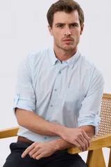 Camisa lisa de algodón celeste, de manga larga con opción de arremangado, cuello camisero, cierre frontal con botones y un bolsillo ojal en el pecho.