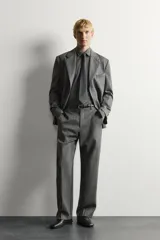 Pantalón de traje gris de corte relaxed fit, confeccionado en pura lana, con bolsillos laterales, bolsillos traseros de doble vivo y raya marcada en las piernas.