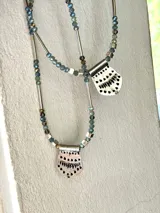 Collar de doble cadena con cuentas de cristal facetado en tonos azules y plateados, con dijes colgantes de metal plateado con diseño calado.