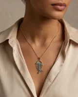 Collar de bronce en tono dorado con una fina cadena y un dije colgante en forma de espina de pescado, decorado con circonias de color turquesa.