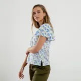 Blusa blanca con estampado de flores azules y verdes, cuello redondo con abertura en forma de gota y mangas cortas amplias.