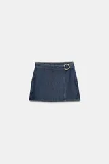 Falda pantalón corta de denim azul oscuro, con diseño cruzado, cierre frontal oculto y hebilla metálica circular en la cintura.
