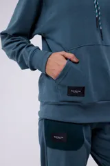 Hoodie azul con capucha y cordón blanco y verde. Tiene un pequeño logo estampado en el pecho y un parche con el logo de la marca en el lateral.