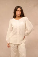 Camisa de algodón color crudo, con mangas largas abullonadas y puños elásticos. Presenta diseño con bordados tipo broderie en toda la prenda y cierre frontal con botones.