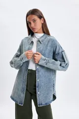Sobrecamisa de jean en tono celeste con efecto lavado, corte oversize, cuello clásico, cierre frontal con botones metálicos y mangas largas con detalle de frunces en los hombros.