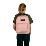 Mochila Jansport modelo Superbreak Plus, color rosa pálido, con compartimento principal y bolsillo frontal con cierre. Presenta asa superior negra y logo rectangular de la marca.