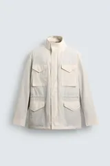 Cazadora técnica de corte relaxed fit, color beige, con cuello subido, manga larga y acolchado interior. Cuenta con múltiples bolsillos frontales con solapa, cintura ajustable con cordón interior y cierre frontal de cremallera oculta por solapa con botones a presión.