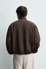 Cazadora bomber reversible de corte relaxed fit, color marrón oscuro, con cuello alto, cierre frontal de cremallera, bolsillos laterales de vivo y acabados elásticos en puños y dobladillo.