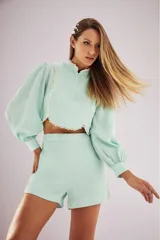 Blusa color verde agua con cuello mao, mangas abullonadas y detalle de perlas en el cuello y en el borde inferior.