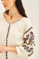 Vestido corto de bambula color celeste, con escote redondo, mangas tres cuartos abullonadas y falda con volado en el ruedo. Presenta bordados decorativos en el frente y las mangas, y cuenta con un cinturón de la misma tela para ajustar a la cintura.