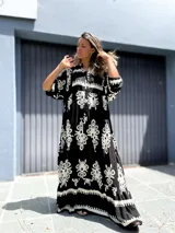 Vestido largo estilo túnica, color negro con estampado ornamental en blanco. Presenta cuello en V con botones y mangas largas amplias.