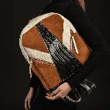 Mochila de cuero vacuno color tostado, con detalles en cuero color arena y negro con textura de cocodrilo. Tiene dos bolsillos frontales con cierre y un bolsillo trasero. El interior está forrado y tiene un bolsillo con cierre y otro pequeño para el celular.