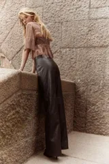 Pantalón de tiro medio en tejido revestido color marrón oscuro, con piernas acampanadas y pliegues cosidos en el frente y la espalda. Presenta cierre y botón frontal, y bolsillos insertados decorativos.