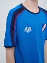 Remera deportiva de entrenamiento Umbro del Club Nacional de Football, color azul marino con detalles en blanco y líneas rojas en los hombros. Cuenta con el logo de la marca y el escudo del club en el pecho.