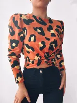 Remera manga larga color naranja con estampado animal print negro y dorado, con nudo en la parte delantera.