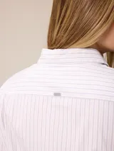 Camisa de corte clásico y calce entallado, color blanco, con cuello camisero, cierre frontal de botones y mangas largas con puños abotonados. Presenta un pequeño bordado distintivo en el pecho.