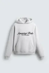 Sudadera con capucha y bolsillo frontal tipo canguro, confeccionada en tejido de algodón con interior perchado. Presenta diseño de corte boxy fit, mangas largas con puños y ruedo en rib, y texto bordado y estampado en el frente.