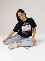 Remera crop negra Under Armour en colaboración con Tini, de manga corta y cuello redondo. Cuenta con un diseño gráfico frontal con el texto "FUTTTURA", fotos estilo polaroid y un listado de canciones en tonos rosados.