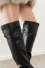 Bota bucanera de cuero negro con caña alta, punta fina y taco cuadrado. Presenta un detalle de hebilla dorada en la parte superior de la caña.